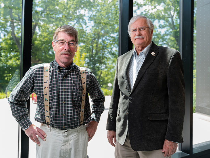 Two men stand in front of glass imprinted with dots to help deter bird collisions.