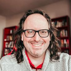 Profile image of man wearing glasses in front of a stack of books.