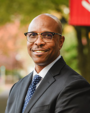 Man standing close to camera wearing dark glasses, suit and tie.