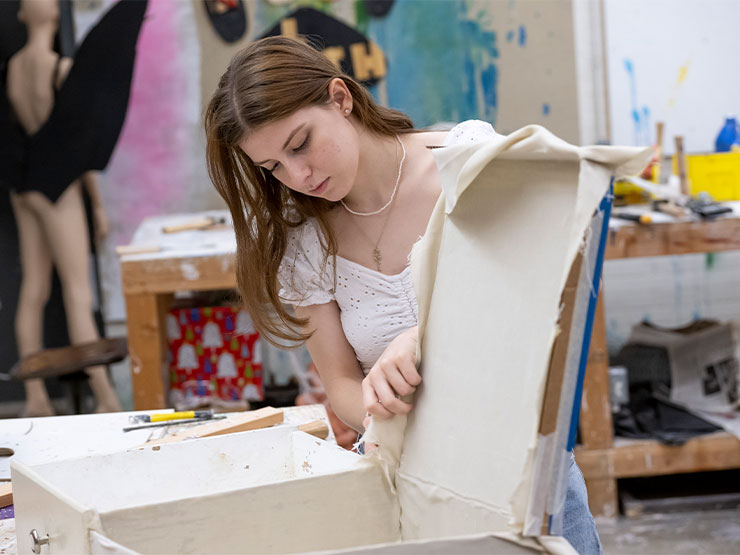 A student affixes fabric to a sculpture in an art studio.