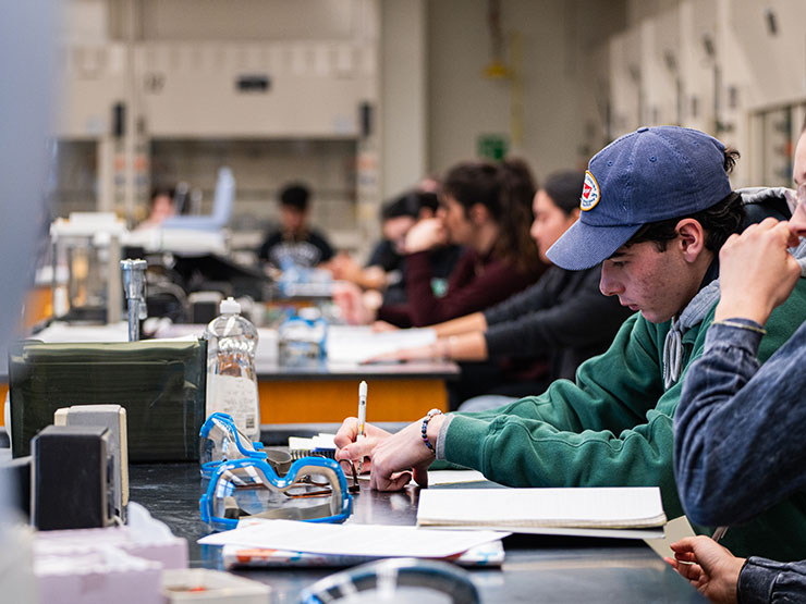 Students write in notebooks at tables in a chemistry lab.