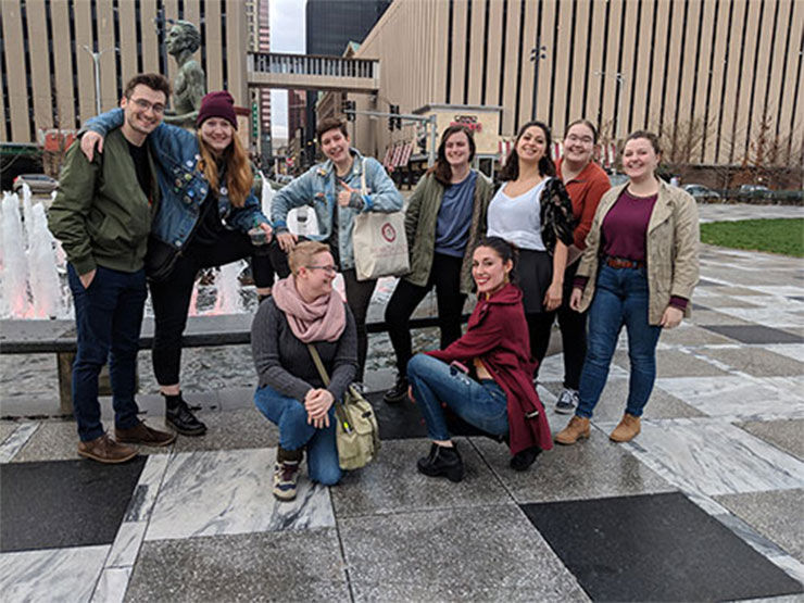 A group of young adults pose for a photo in a park among city buildings.