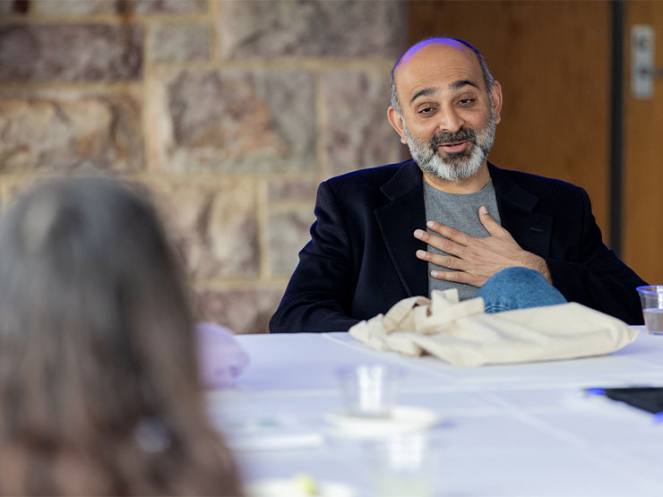 An adult author speaks to a group of students, his hand resting on his chest.