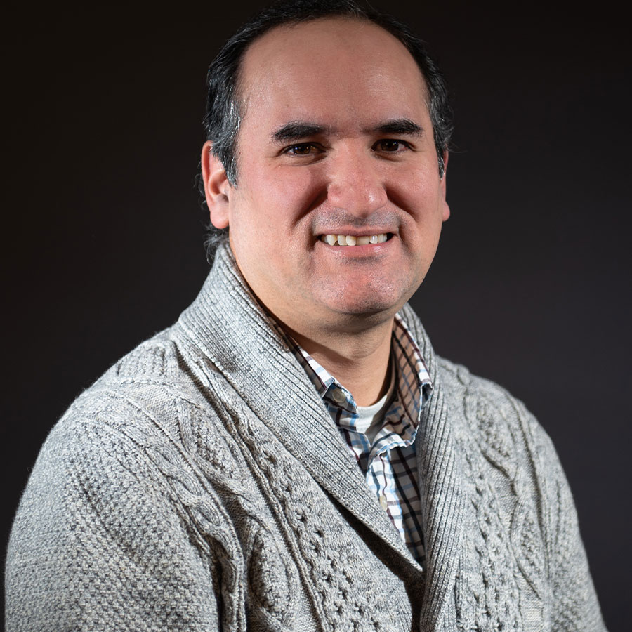 A man in a grey sweater smiles against a black backdrop.