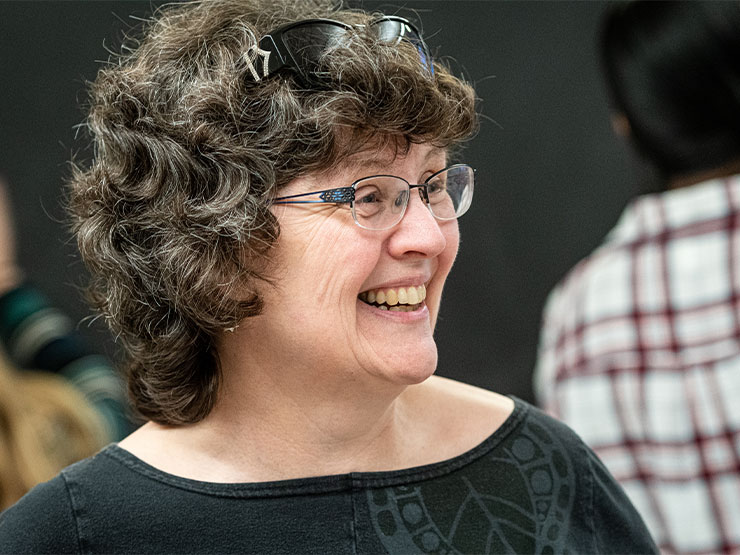 An instructor with short, curtly hair and glasses grins in a classroom.