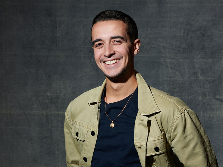 A professional headshot of a smiling young adult in a green jacket and black shirt.