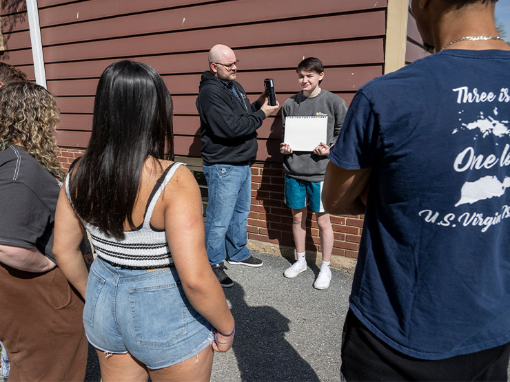 Students stand outside while an instructor demonstrates production lightning tips.