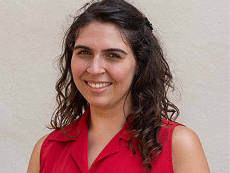 A recent college graduate wearing a red sleeveless blouse smiles at the camera.