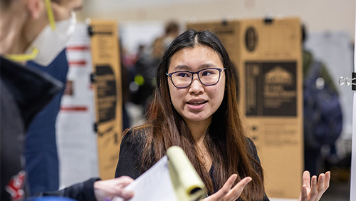 A student speaks to someone off-camera at a poster session for student research.