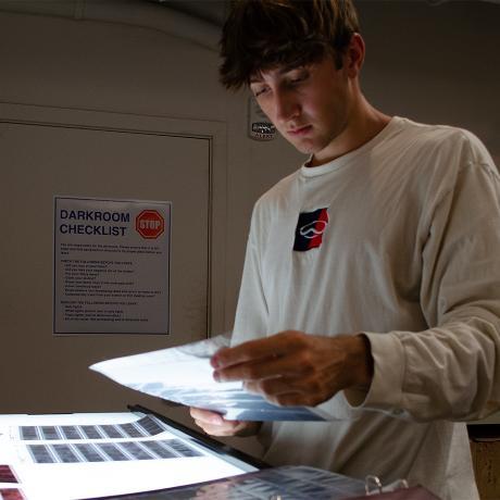 A student flips through photography negatives inside a dark room.