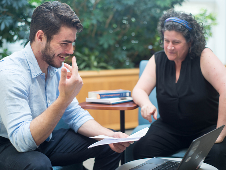 A students laughs and talks with an instructor as they review a document together.