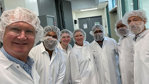 A group of people in lab coats and hair nets smile inside a laboratory.