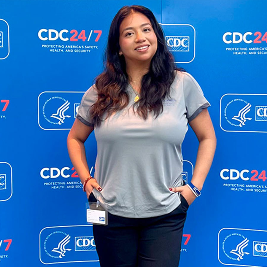 A smiling college student stands against a backdrop with logos for the Centers for Disease Control.