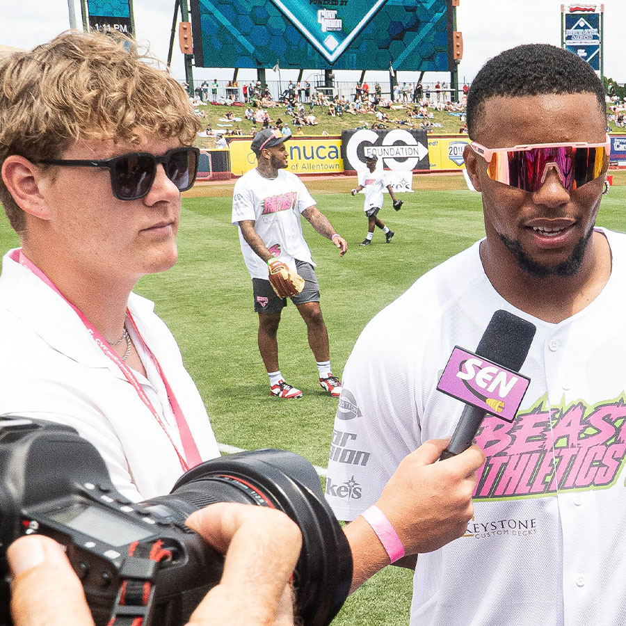 A college student with sunglasses interviews an athlete for a television broadcast.