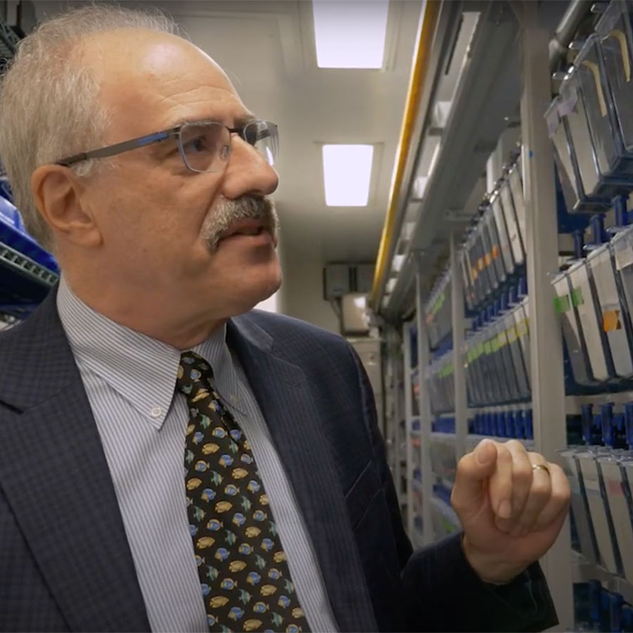 A scientist in a suit and tie stands in a room full of fish tanks