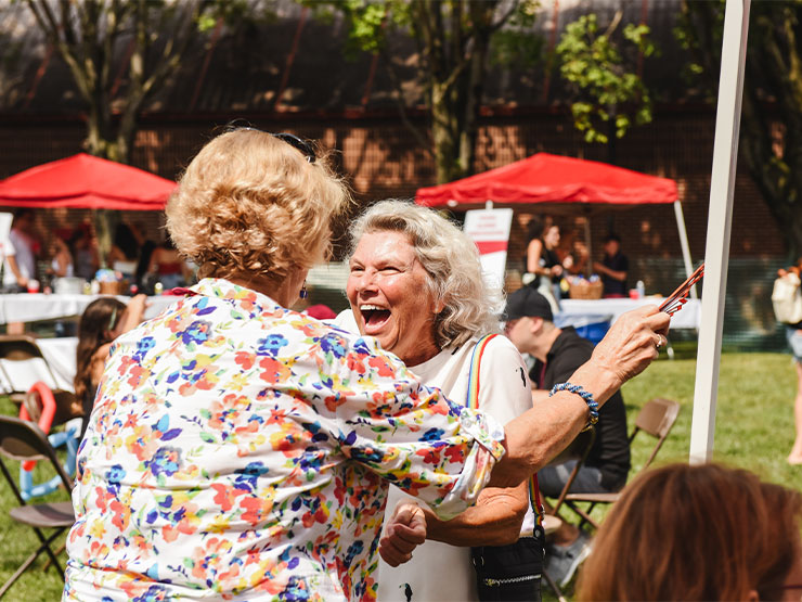 Two older adults hug enthusastically on a college campus.