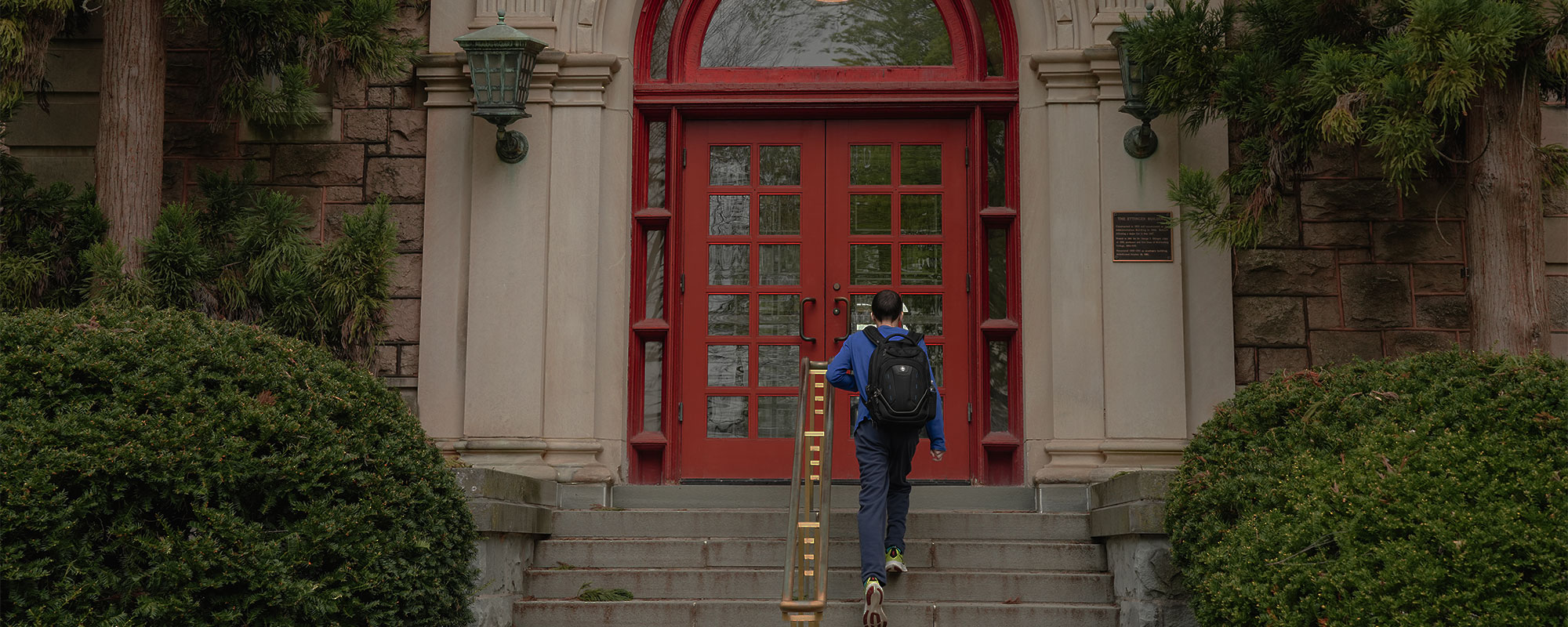 A college student walks up the stairs of the Ettinger building at Muhlenberg College and toward a pair of red double doors.