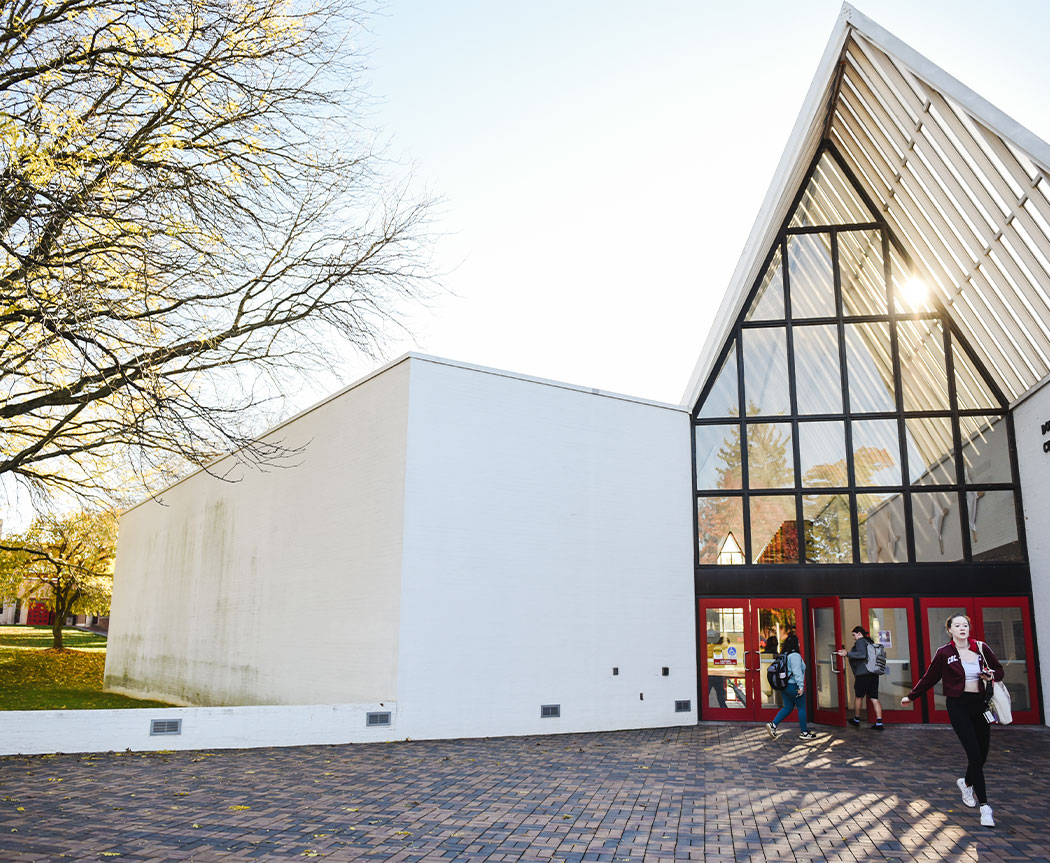 Sunlight is reflected in the glass of the Baker Center for the Arts at Muhlenberg College, a white, modern building.