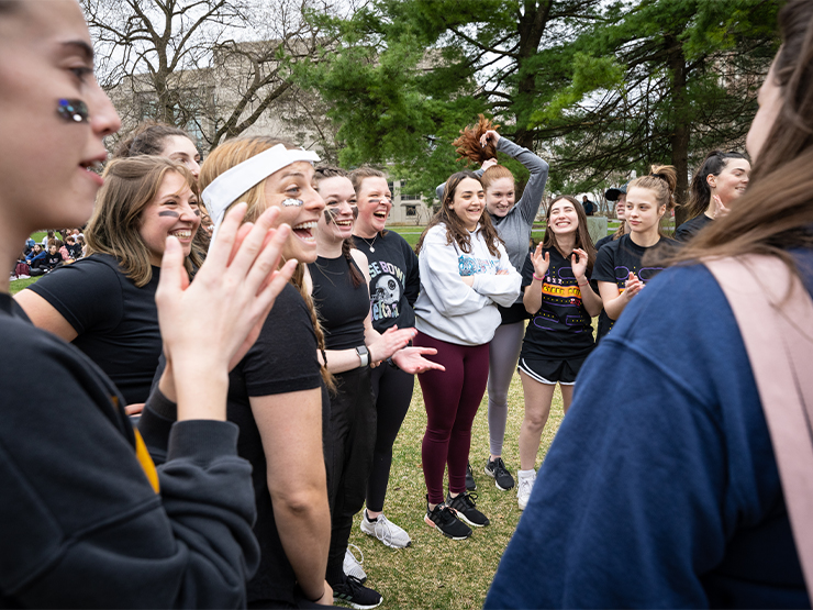 A group of students stand in a circle, clapping and cheering.