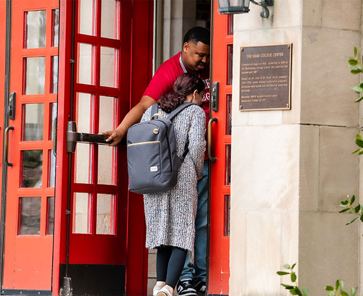 Someone holds open a red door at Haas College Center for a student entering the building.