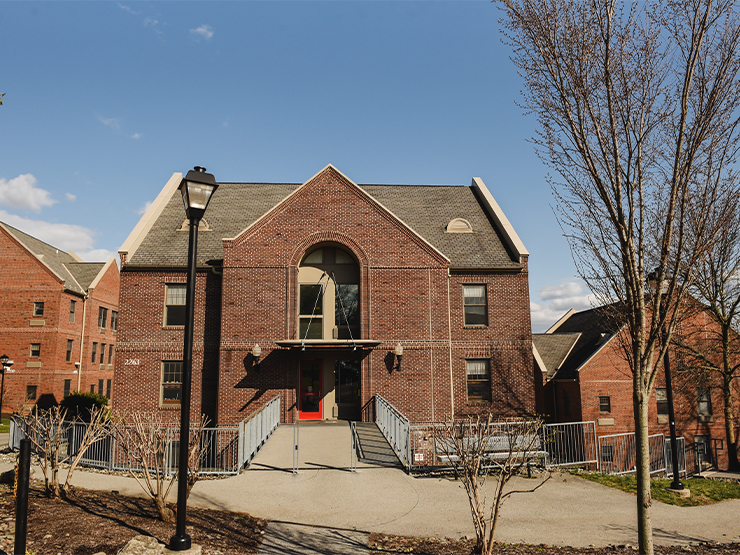 A cluster of brick buildings that serve as off-campus housing sit under a blue spring sky.