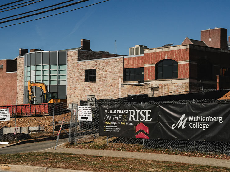 Fencing and signage surround the Seegers Union building at Muhlenberg College with construction vehicles nearby.