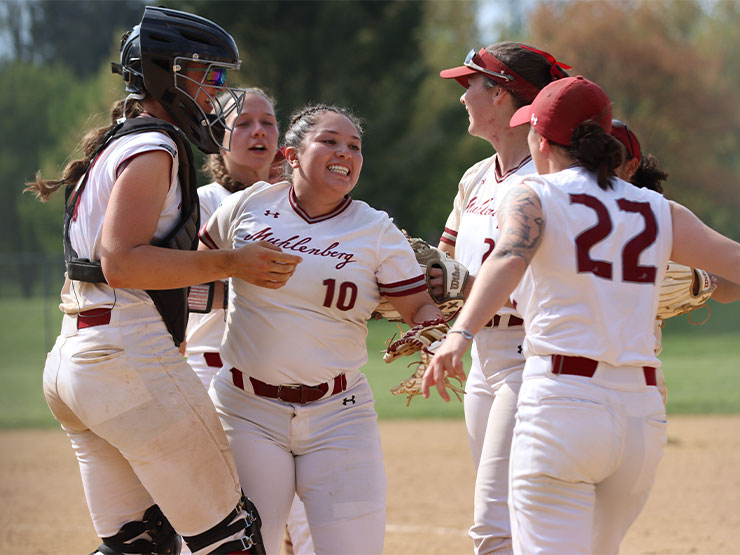 A group of Muhlenberg softball players run toward each other in celebration on a ballfield.