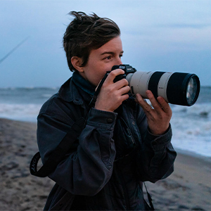 A person holding a camera on the beach.