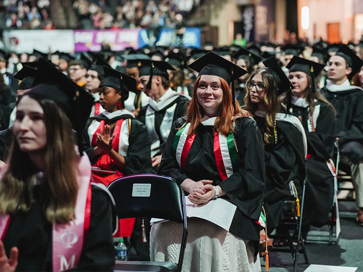 Students in graduation regalia are seated in a commencement ceremony.