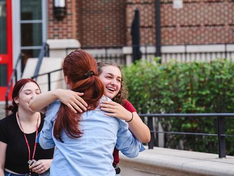 Student wearing blue shirt embracing another student.