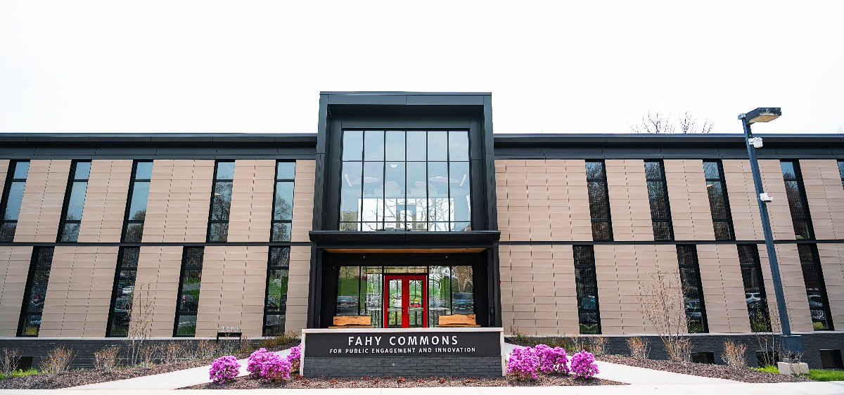 A front view of a modern building with large windows and flowering bushes in front..