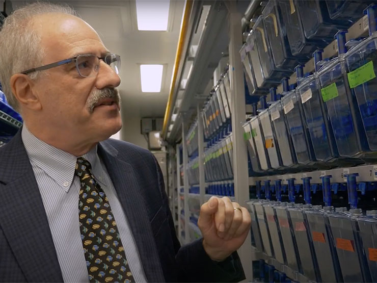 A scientist in a suit and tie stands in a room full of fish tanks.