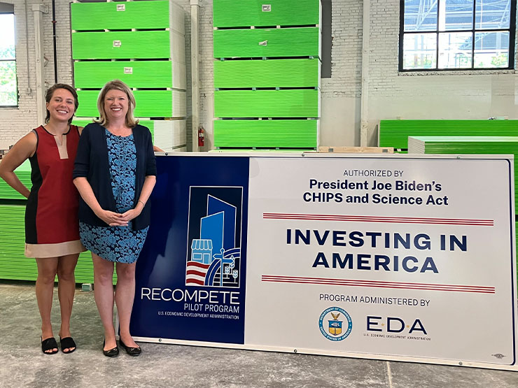 Two individuals stand beside a large sign that reads Investing in America.