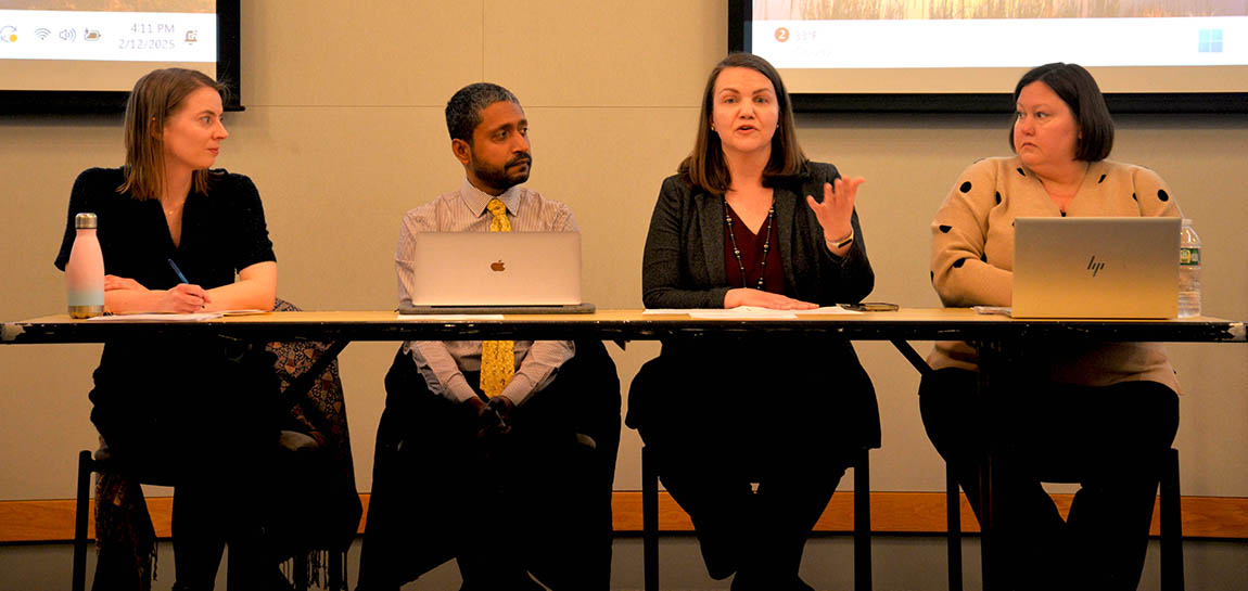 A panel of four college faculty members sits at a table in front of a room