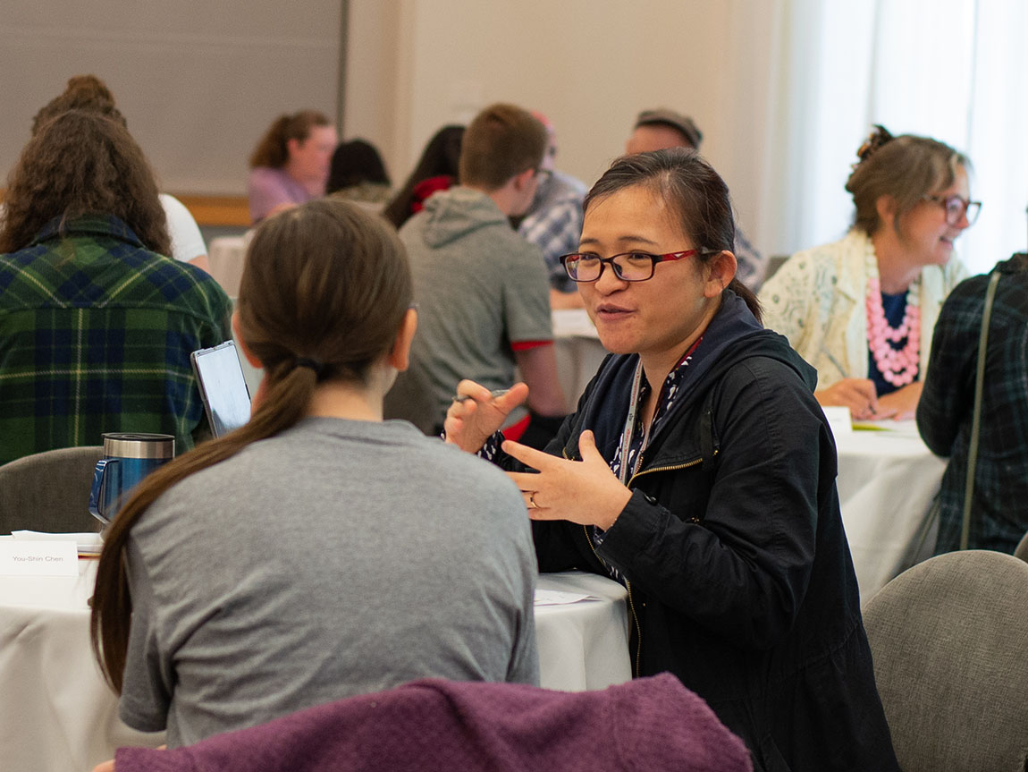 A college professor sits with a student and talks animatedly