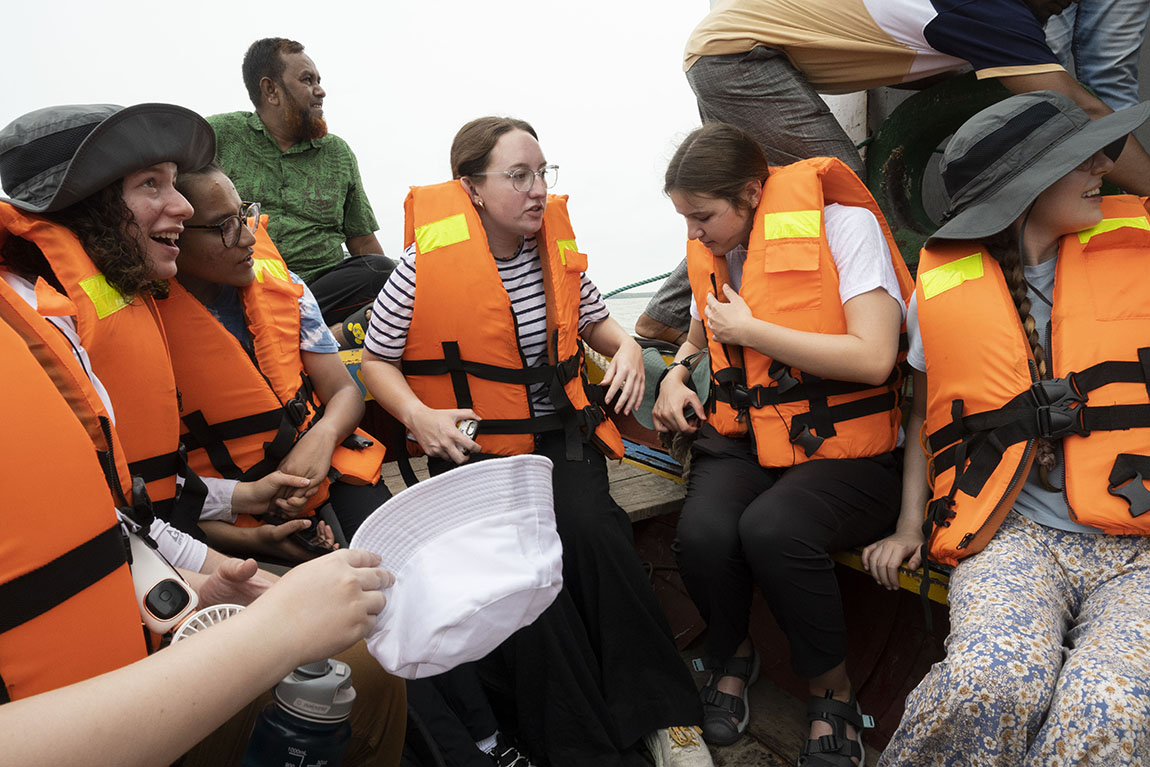 A group of college students wearing orange life vests in a small boat