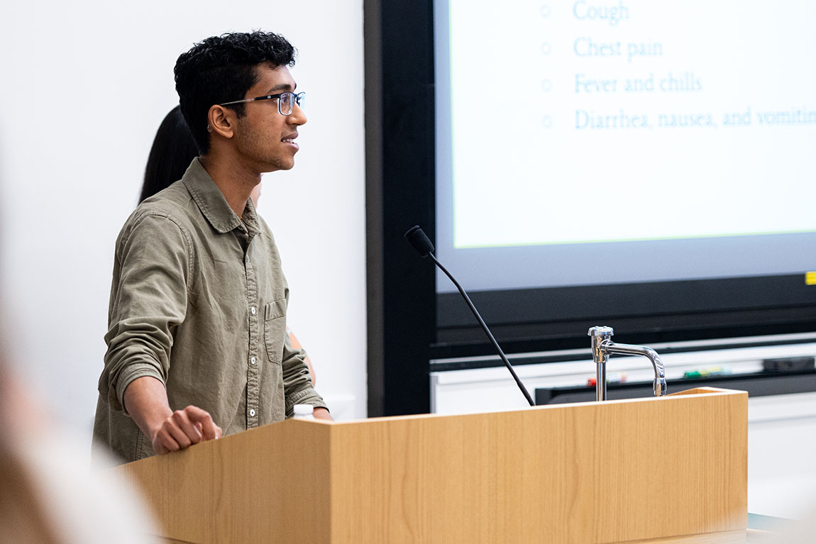 A college student wearing glasses stands at a podium