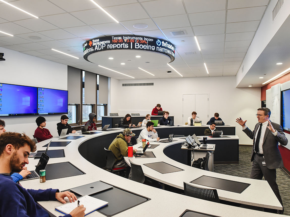 College students attend class in a modern classroom with a stock ticker on the ceiling