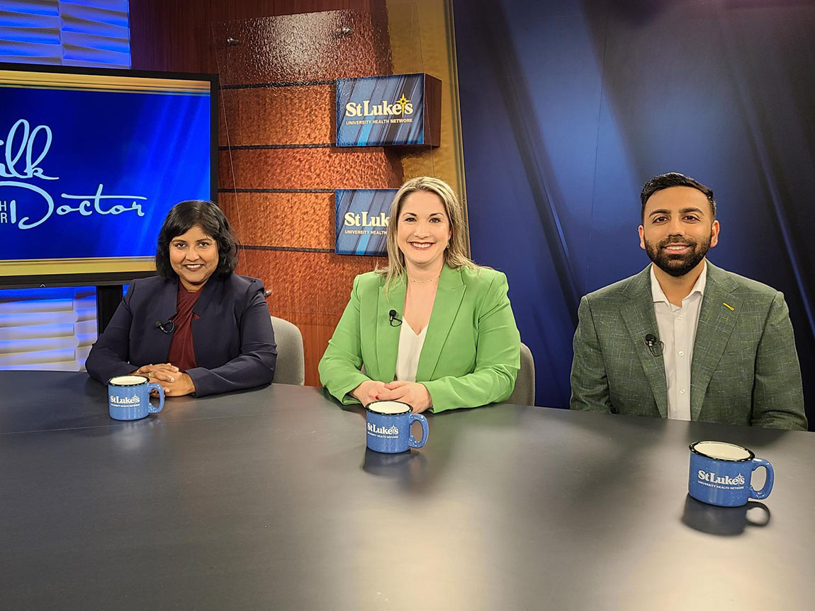 Three people sit at a table and smile before filming a TV show