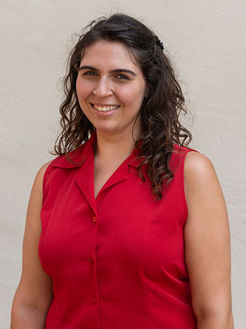 A young woman with dark curly hair and a red shirt smiling in front of a white background