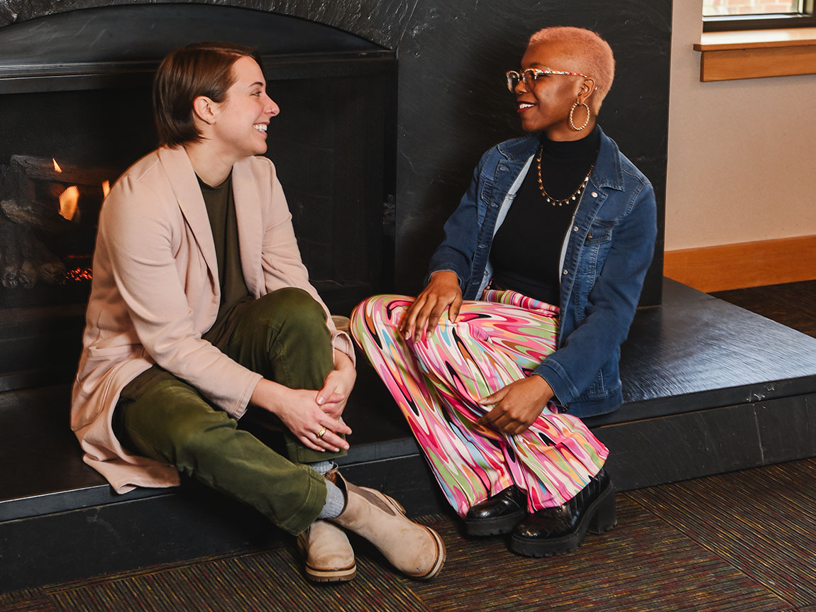 A college librarian and a college student sit by a fireplace and talk