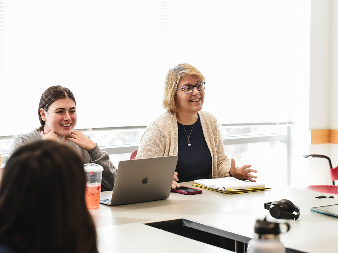 A college professor in glasses smiles while teaching a class