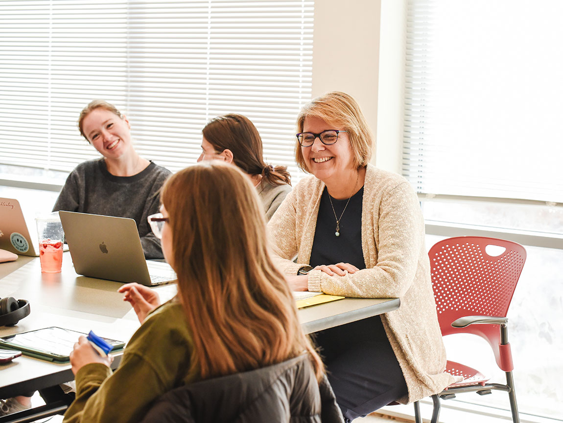 A college professor smiles at a student while they're both seated during a class