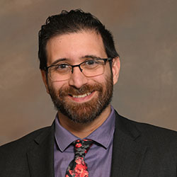 A headshot of a college professor with a beard, glasses, and a flowered tie on