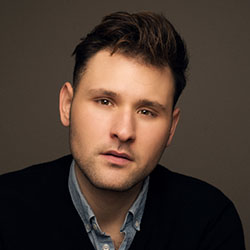 A headshot of James Stabp, who has dark hair and a collared shirt under a blazer on