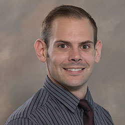 A headshot of a college professor with dark hair and a collared shirt on