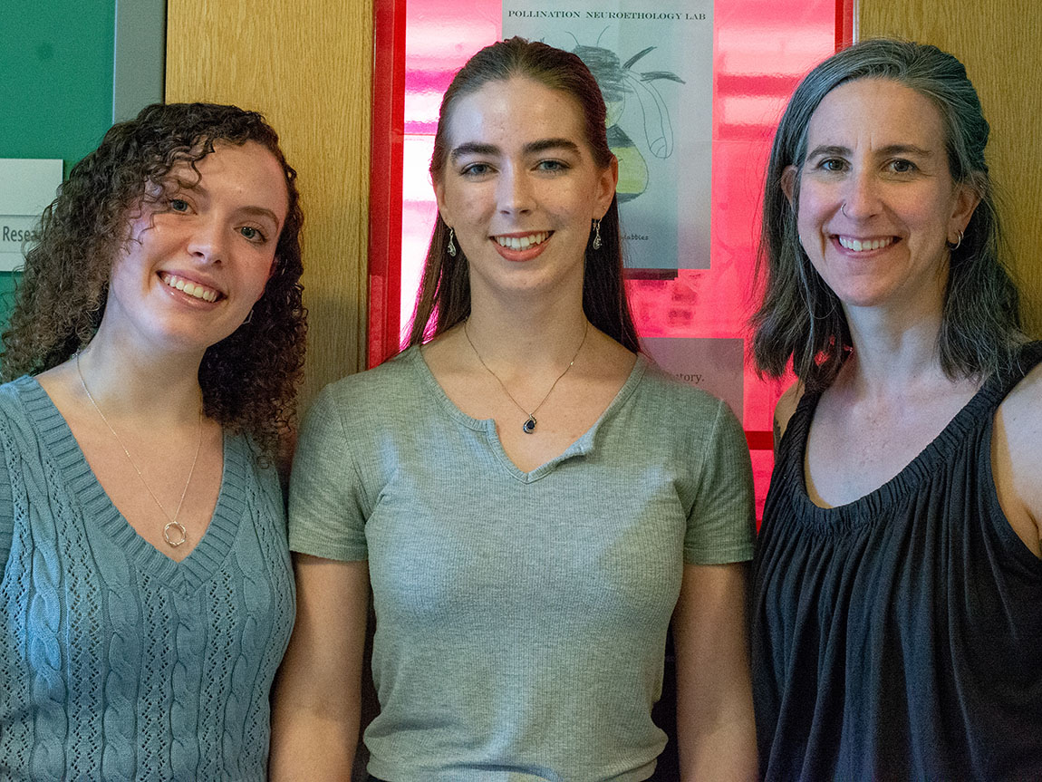 Two college students and a neuroscience professor stand outside a door