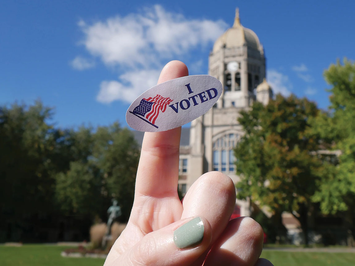 A finger with an I Voted sticker on it with the Haas Bell Tower in the background