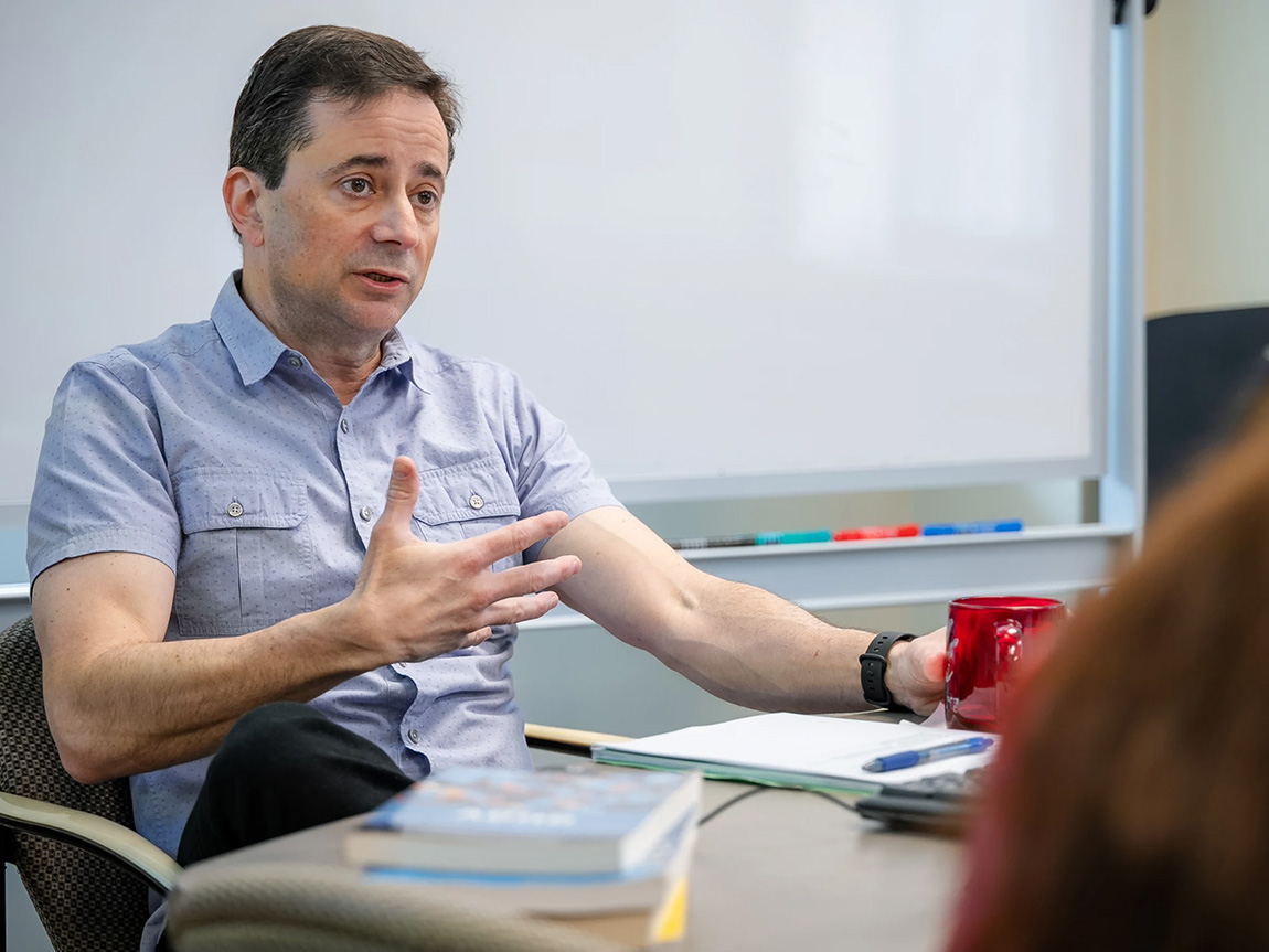 A college professor in a blue shirt speaks during class
