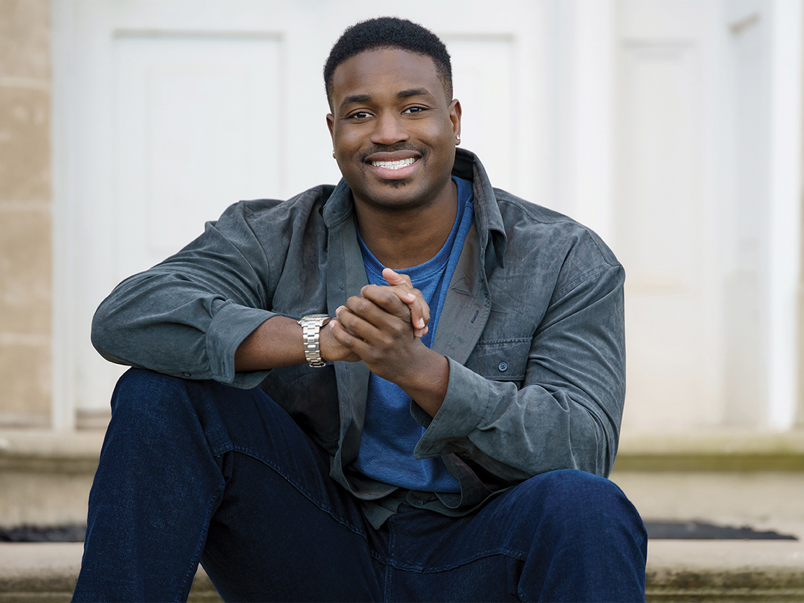 A headshot of a young man sitting outside wearing blue clothing